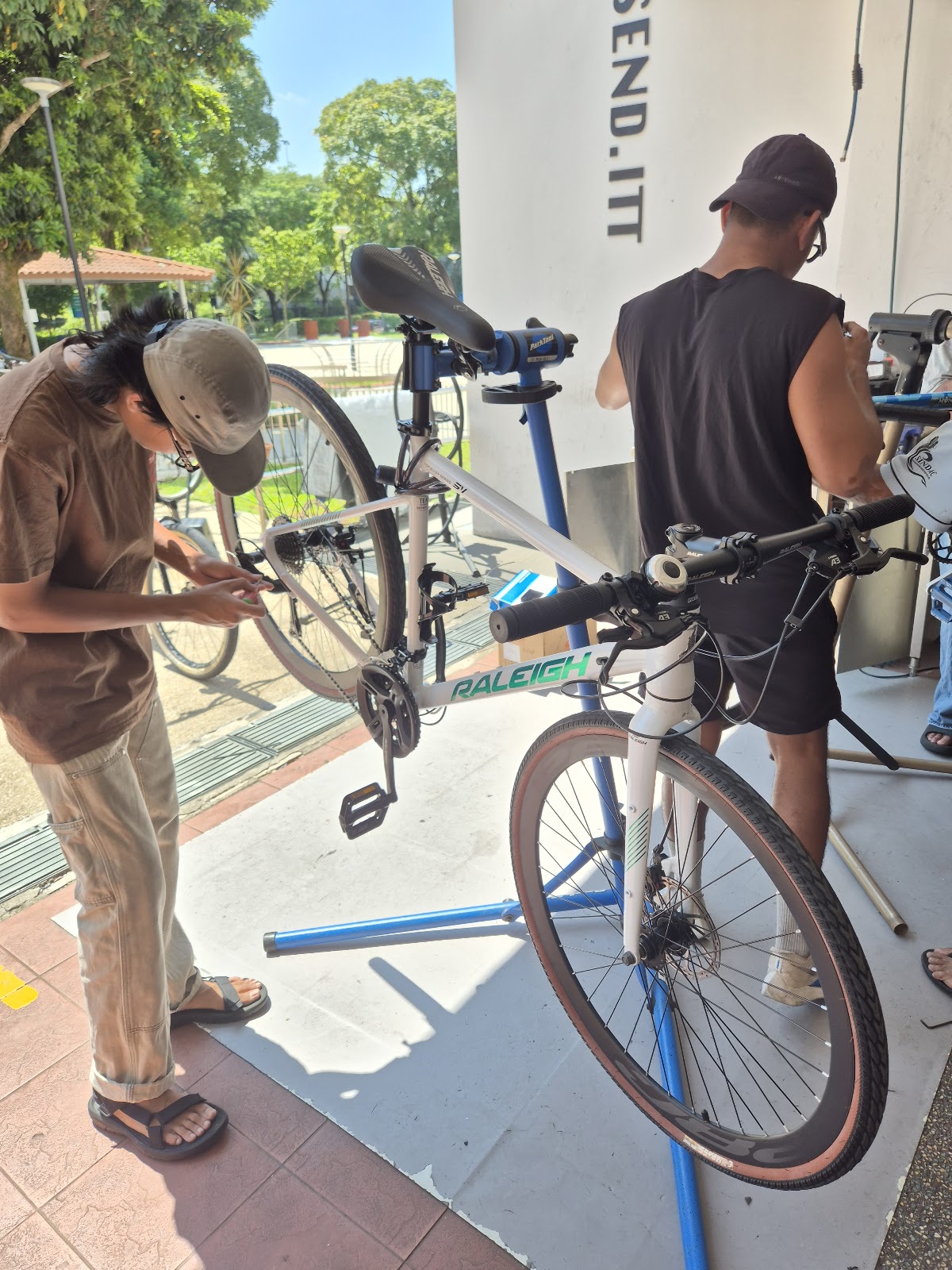 Two mechanics servicing a Raleigh hybrid outside the Send Itt shopfront